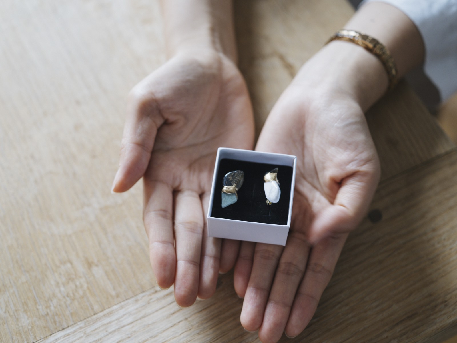 Hands holding a boxed pair of kintsugi accessories joined with gold