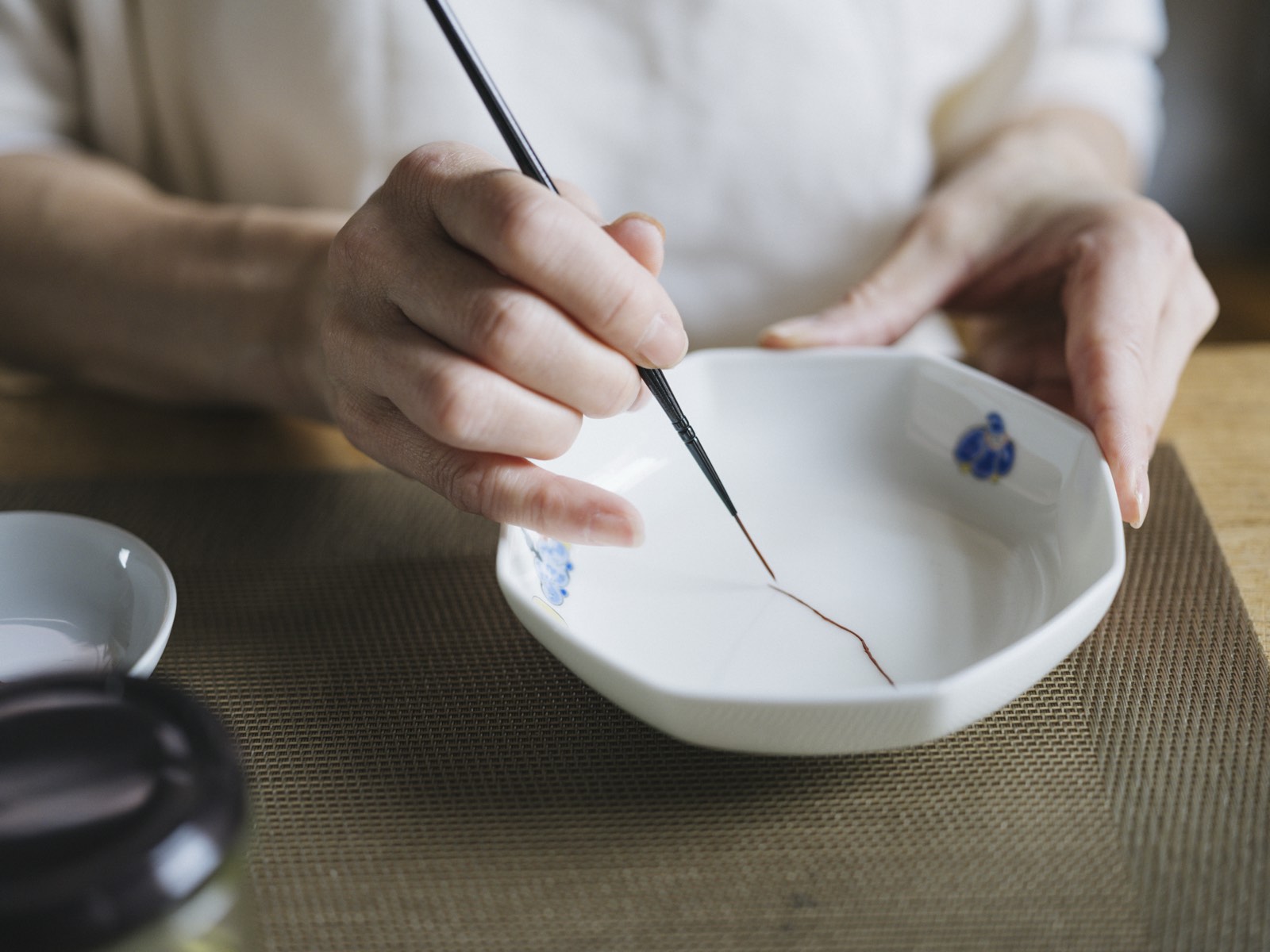 A fine brush drawing a golden seam along a delicate dish