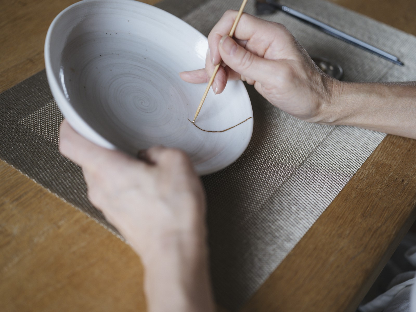 Hands drawing a golden seam along a mended bowl